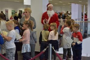 Na zdjęciu jest mężczyzna przebrany za świętego mikołaja i dzieci zwracające swoje twarze ku niemu. W tle starsza kobieta patrząca przed siebie.