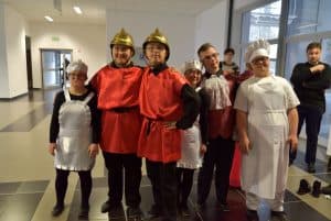 Ludzie stojący w sali i uśmiechający się do zdjęcia. Są ubrani w stroje strażaków i kucharzy.