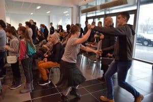 Ludzie stojący na widowni i patrzący na wprost siebie. Po lewej stronie mężczyzna tańczący z kobietą.