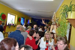 Grupa ludzi znajduje się na sali. Sala jest dosyć ciasna. Dwie kobiety całują się ze sobą.