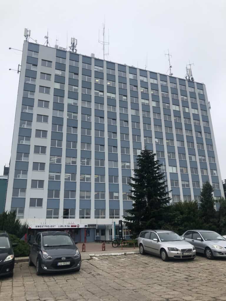 Dziesięciopiętrowy biurowiec, obok parking.