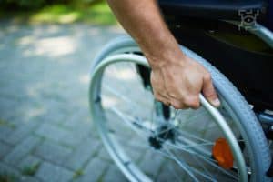 Zbliżenie na dłoń mężczyzny przytrzymującą obręcz koła wózka inwalidzkiego