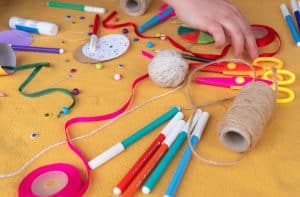 Zbliżenie na rozłożone przybory plastyczne: kolorowe flamastry, nożyczki, klej, wstążki, sznurki jutowe