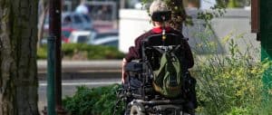Osoba na wózku inwalidzkim ze stabilizacją głowy na licy zwrócona tyłem do obiektywu.