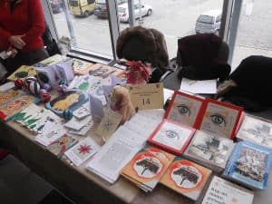 stół z różnymi broszurami, malunkami, kolorowymi piłeczkami, drobnymi rękodziełami.