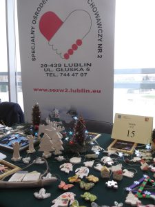 stół zastawiony rękodziełami i pracami plastycznymi. W tle baner z adresem ośrodka. Na dole banera informacja o stronie internetowej - www.sosw2.lublin.eu