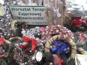 Na zdjęciu prace manualne: wianki świąteczne, aniołki. Obok nich postawiona jest tabliczka “ Warsztaty Terapii zajęciowej “Misericordia”.