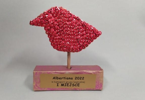 Ptaszek cekinowy w kolorze czerwonym na podstawce z nadrukiem Albertiana 2022 w kategorii grupy teatralnej I MIEJSCE