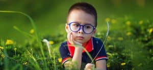 Chłopczyk w okularach z niebieskimi oprawkami na tle zieleni, podpiera twarz prawą rączką.