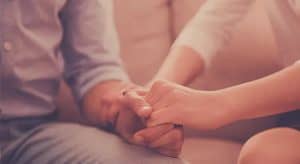 Zbliżenie na dłonie kobiety przytrzymującą dłoń mężczyzny w geście wsparcia.