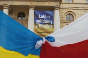 Związane rogami flagi Polski i Urainy, za nimi front budynku ratusza z plakatem: Lublin solidarny z Ukrainą #StandWithUkraine