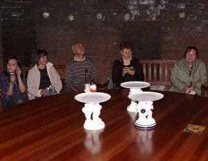 Ludzie siedzą przy stole. Na stole są trzy tace. Ludzie uśmiechają się.