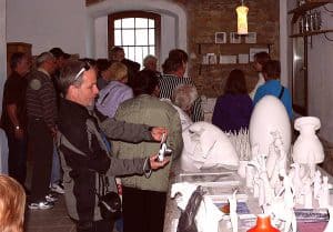 Ludzie stoją przy stole z wyrobami manualnymi. Jeden mężczyzna trzyma aparat w dłoniach.