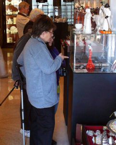 Ludzie stoja przed szklaną witryną. Jedna z kobiet wyciąga wskazujacy palec w kierunku witryny.