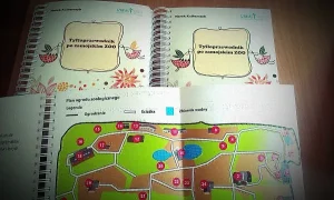Na zdjeciu jest mapa ogrodu zoologicznego w skoroszycie. W tle skoroszyty z tekstem tyfloprzewodnik po zamojskim zoo