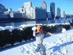 Chłopiec rzuca kulkę śnieżną przed siebie. W tle śnieg i budynki.