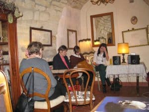 Ludzie siedzą na krzesłach. Kobieta w tle ma założoną dłoń na twarz. Na ścianach wiszą ramy obrazów bez zdjeć.