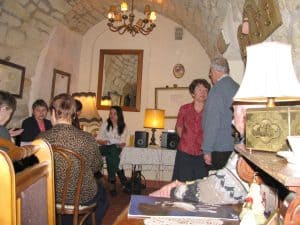 Ludzie są w kawiarni. Niektórzy siedzą przy stolikach inni stoją. Twarze ludzi są zwrócone ku sobie