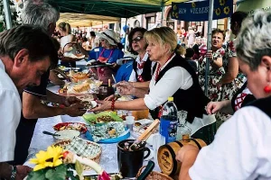 Ludzie nachylajacy sie do stoiska z jedzeniem. Kobieta i mężczyzna trzymają talerz nad stołem.