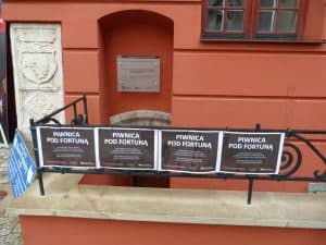 Jest budynek. Wyjście do budynku jest od strony piwnicy. Na balustradzie są powieszone plakaty “piwnica pod fortuną”.