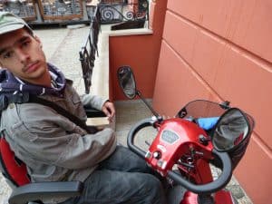 Mężczyzna siedzi na wózku inwalidzkim elektrycznym. W tle są schody do sutereny.