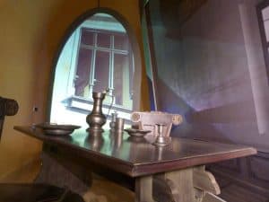 Stół z krzesłami. Na stole są naczynia. W tle jest okno.