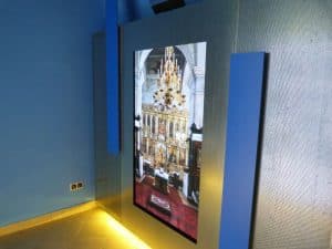 Zdjęcie wisi na ścianie. Dół ściany jest podświetlony ledami. Na zdjęciu jest wnętrze kościoła.