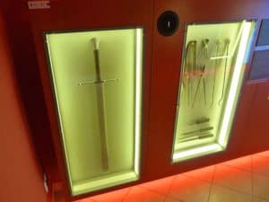Na ścianie w szklanych szybach są narzędzia bitewne - m.in. miecz. Szklane szyby są podświetlone ledami.