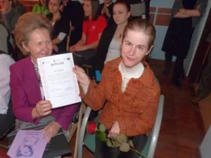 Kobiety siedza. W dłoniach razem trzymaja dyplom. Uśmiechają sie do zdjęcia.