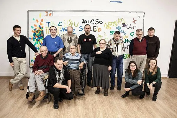 Ludzie stoją w grupie. Pozują do zdjęcia. Niektórzy są na wózkach. Uśmiechaja sie do zdjecia.