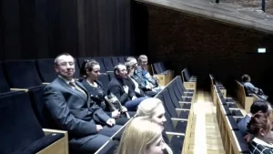 Ludzie siedzą na widowni. Uśmiechaja sie do zdjecia.