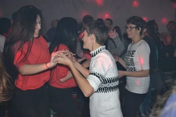 Ludzie tańczą i trzymaja się za ręce. Są kolorowe światła