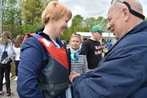 Kobieta i mężczyzna stoją naprzeciwko siebie. Kobieta ma na sobie kapok, a mężczyzna ma wyciągnięte ręce w jej stronę. Oboje uśmiechają się.