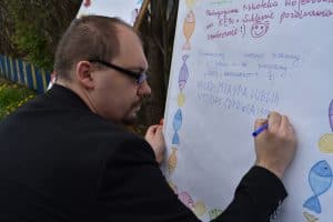 Mężczyzna stoi przed tablica i trzyma flamaster. Na tablicy widnieje napis: “ Pedagogiczna Biblioteka Wojewódzka im. KEN w Lublinie pozdrawia serdecznie. Pozdrawiamy i mocno ściskamy, a i gorące buziaki przesyłamy “ŚDS ABSOLWENT”, URZĄD MIASTA LUBLIN WYDZIAŁ ZDROWIA I “.