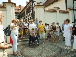 Ludzie stoją w grupie na deptaku. Uśmiechaja się. Ich twarze sa skierowane ku sobie