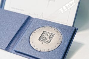 W niebieskiej oprawie jest medal Prezydenta Lublina. Na środku herb miasta.