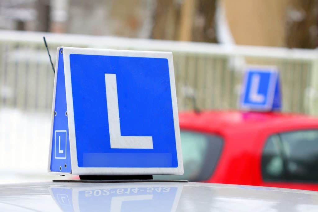 Identyfikator auta do nauki jazdy “L”. w tle inne auto z “L”.