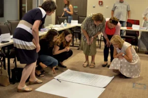 Kobiety pochylają się nad kartkami które leżą na podłodze.