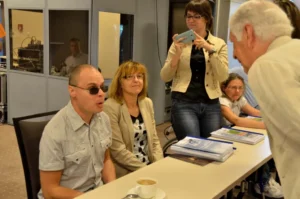 Ludzie siedzą przy stole. Na stole jest kawa i książki.