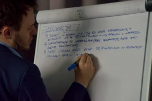 Mężczyzna stoi przy tablicy papierowej. W dłoni ma mazak.