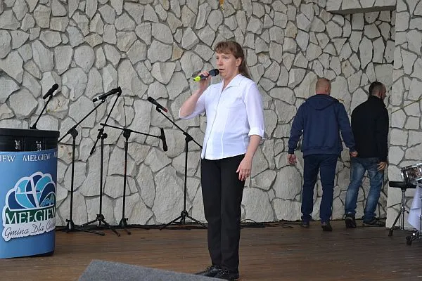 Kobieta stoi na scenie. W dłoni mikrofon