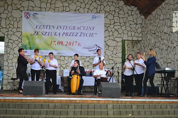 Ludzie stoja na scenie. W dłoniach mają instrumenty