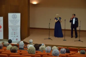 Kobieta stoi na scenie. Obok niej mikrofon. obok także mężcyzna