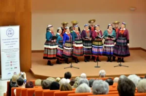 Ludzie są na scenie w kolorowych strojach. W dłoniach trzymają teczk.
