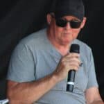 Mężczyzna w czarnej czapce i ciemnych okularach trzyma w ręku mikrofon