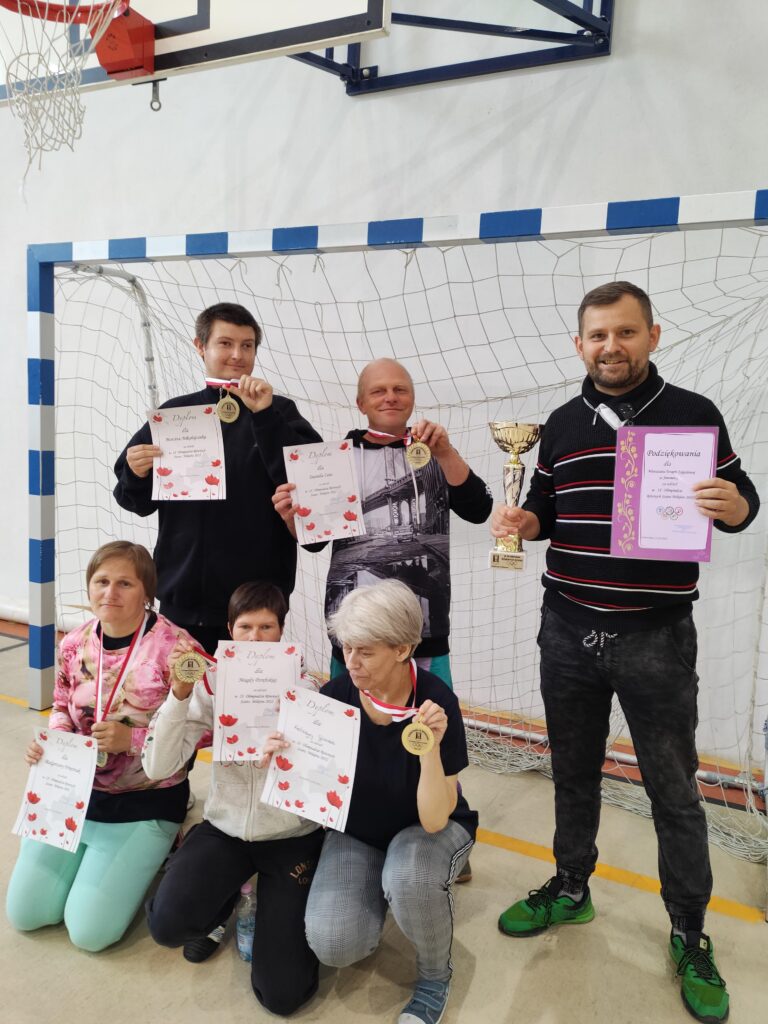 Trzy kobiety kucające i trzech mężczyżn stojących za nimi prezentują otrzymane medale, dyplomy i puchar.