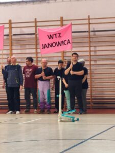 Ośmioosobowa drużyna trzymająca różowy transparent z czarnym napisem WTZ Janowica.