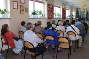 Zgromadzeni uczestnicy siedzący na krzesłach zwróceni tyłem do aparatu.