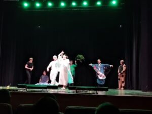 Siedmioro uczestników rozgrywa przedstawienie na scenie.