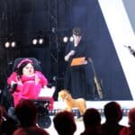 Trzy osoby na scenie, od lewej: siedząca na wózku inwalidzkim Pani Bogumiła Siedlecka-Goślicka oraz stojący przedstawiciele Integracji, członkowie Jury konkursu na Dostępny plac zabaw „Inte-GRA”: Pani Katarzyna Rzehak i Pan Kamil Kowalski; widok z widowni